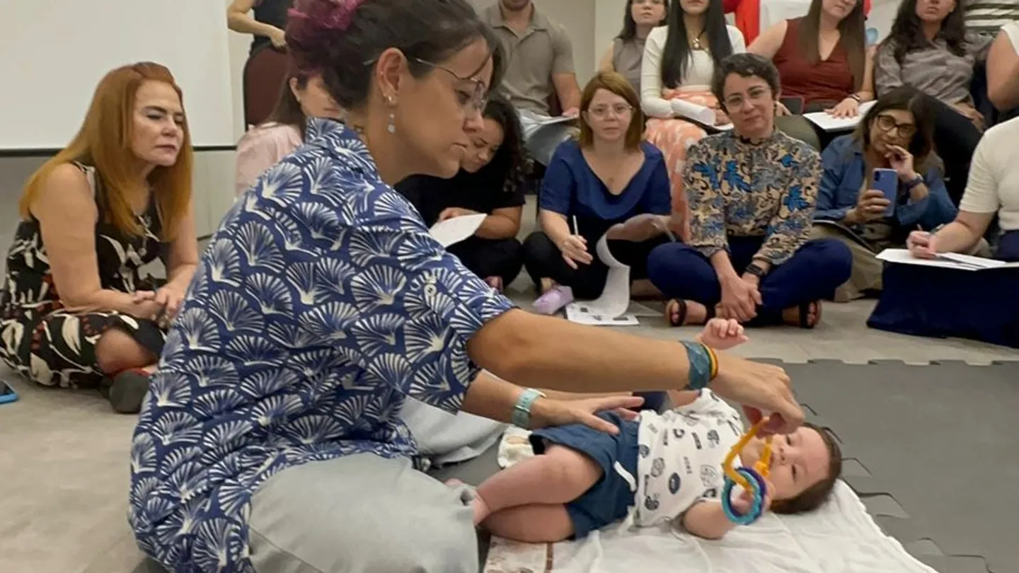 Profª Drª Dafne Herrero demonstrando o manejo de um bebê diante de uma plateia de fisioterapeutas