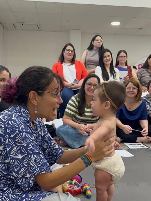 Dafne apoiando um bebê em pé, diante de uma turma de fisioterapeutas