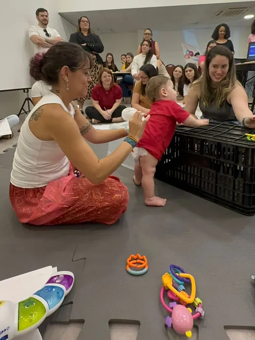 Dafne apoiando uma criança em pé diante de uma plateia de profissionais