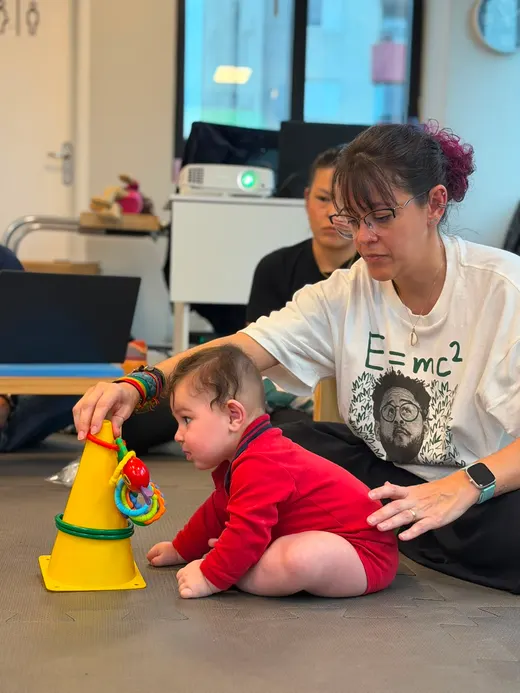 Dafne oferecendo um brinquedo a um bebê sentado no chão