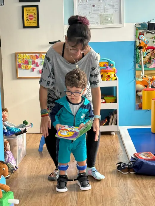 Dafne apoiando uma criança em pé numa sala de atendimento